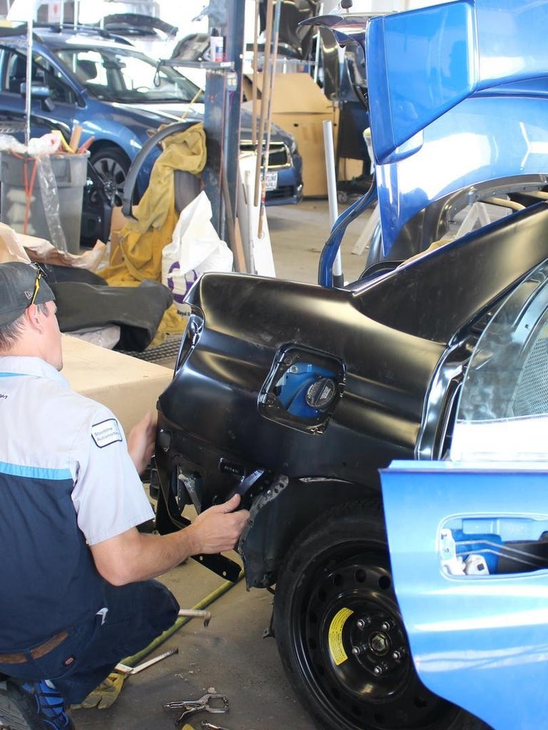 A Collision Repair specialist removing a dent from a passenger-side door