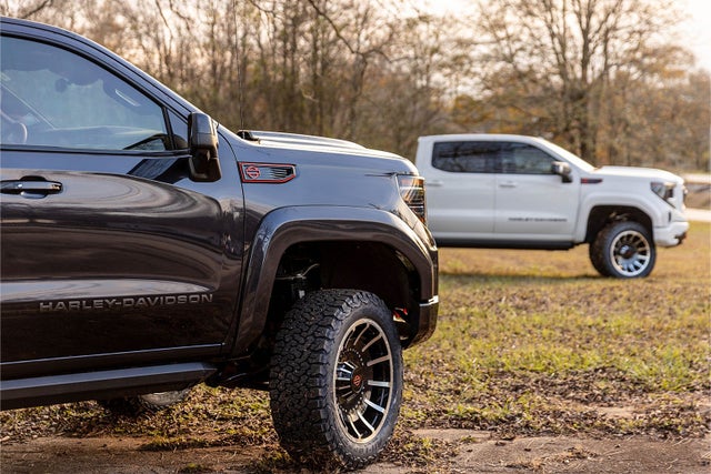 Two GMC Sierra 1500 Harley Davidson Lifted Trucks parked in a tree-lined clearing