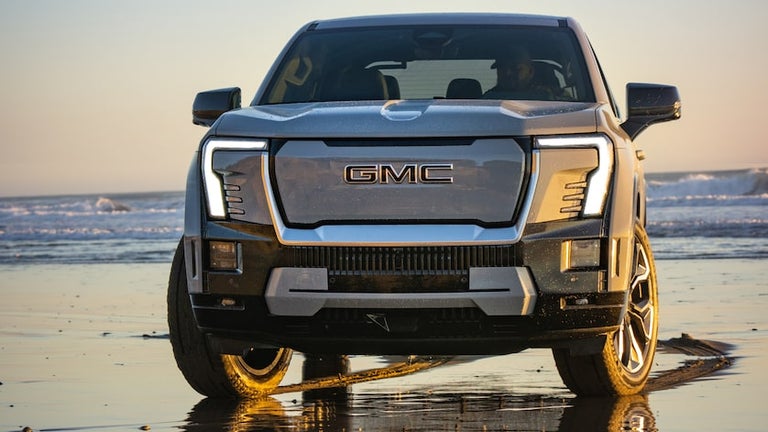 Front View of the GMC Sierra EV Denali Driving on the Beach at Sunset