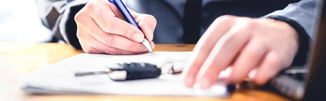 A man signing a document with a key fob on top of the paper